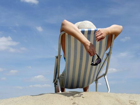 Woman sunbathing on deckchair on the beach shot against blue skyの写真素材