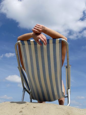 Woman sunbathing on deckchair on the beach shot against blue skyの写真素材