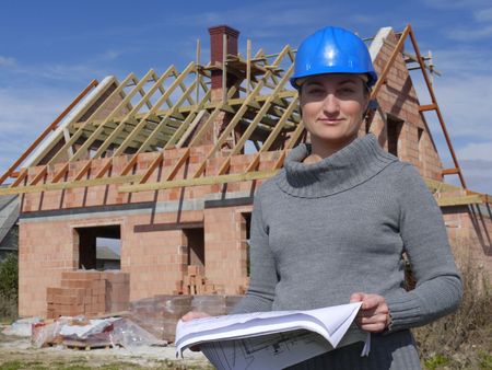 Female architect wearing blue helmet posing with building plans against unfinished brick houseの写真素材