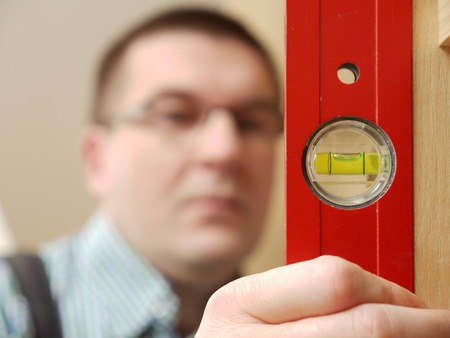 Closeup shot of carpenter looking at spirit level gauge to check verical positioning of furniture - shallow depth of fieldの写真素材
