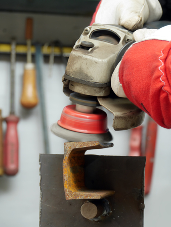 Closeup of machinist worker hands brushing a metal piece using wire brush on angle grinderの写真素材