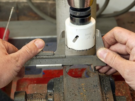 Closeup of machinist worker hands taking a diameter measurement of hole cut in a metal piece using calliperの写真素材