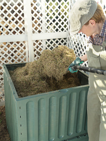 Female gardener turning over compost bin content using pitchfork to speed up decomposting process