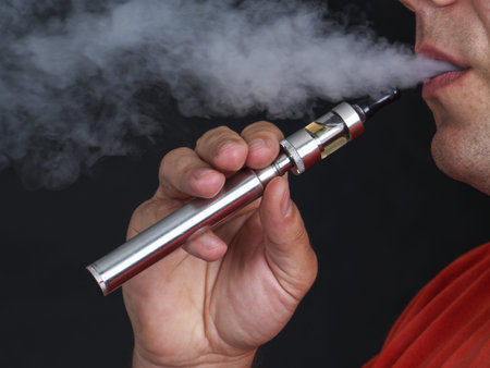Closeup of man using e-cigarette and exhaling vapor shot over black background