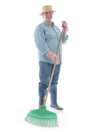 Senior woman gardener wearing straw hat and rubber boots posing with plastic lawn rake over white の写真素材