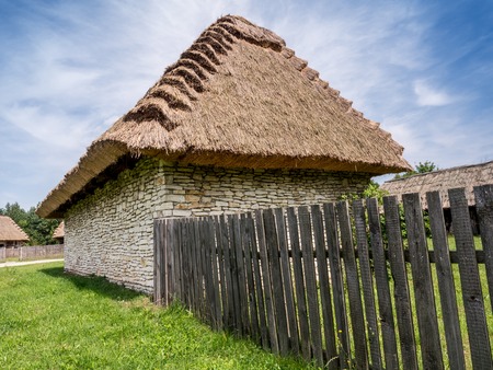 Farmstead with thatched cottage and picket fence shot against blue skyのeditorial素材