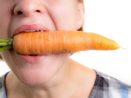 Woman holding a fresh carrot in her mouth