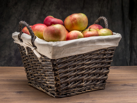 Wicker basket full of delicious apples shot over dark gray backgroundの写真素材