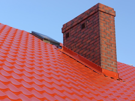 Closeup of red roof metal covering with brick-made chimneyの写真素材
