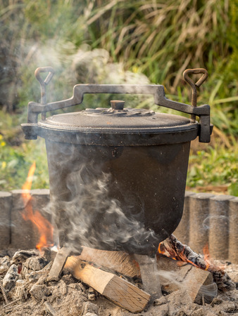 Black cast-iron kettle with fare placed on fireの写真素材