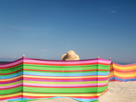 Female sunbather in straw hat relaxing on the beach behind windbreakの写真素材