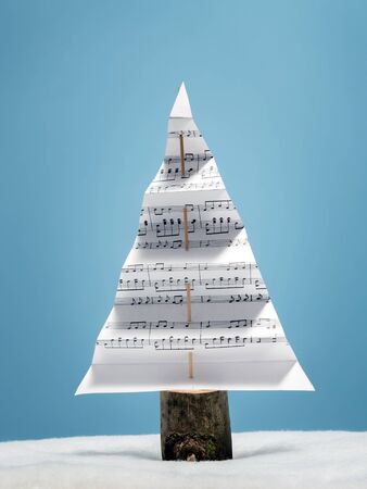 Paper christmas tree with christmas carol notes over light blue backgroundの写真素材