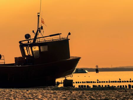 Silhouette of the fisherman's boat docked at the sandy wharf against the sunset skyの写真素材