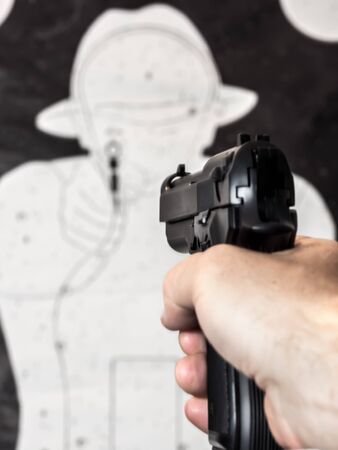 Closeup of man's hand holding pistol aiming at the paper silhouette targetの写真素材