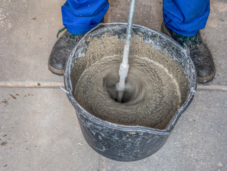 Construction worker mixing mortar in a bucket using handheld concrete mixerの写真素材