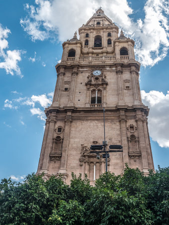 A magnificent historic cathedral bell tower rising majestically above a cityscape, bathed in sunlight beneath a clear blue sky, Murcia, Spainの写真素材
