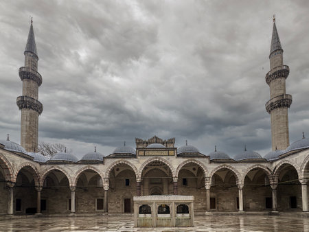 Intricate architecture of a mosque courtyard, flanked by lofty minarets, under a dramatic cloudy sky, reflecting the rich cultural and historical significance of the structure., Istanbul, Turkeyの写真素材