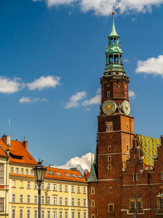 A vibrant scene featuring a historic Townhouse with clock tower surrounded by charming colorful buildings under a sunny, cloud-dotted blue sky, Wroclaw, Polandの写真素材