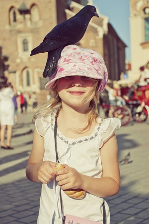 Little girl with pigeon on the head in old town squareの写真素材