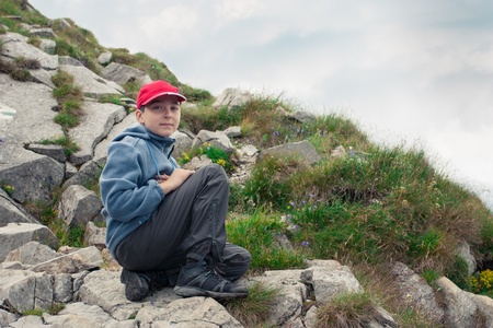 Boy resting on mountain trail  Rocks and cloudy sky in backgroundの写真素材
