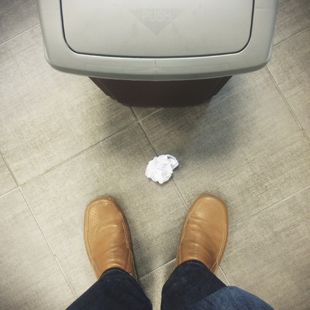 Man standing next to rubbish bin and crumpled piece of paperの素材