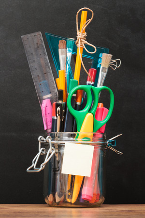 School accessories in jar on desktop with blackboard in the backgroundの写真素材