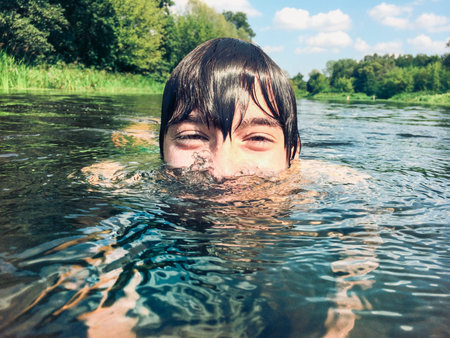 Young boy splashing in the water. Green at the background.の素材