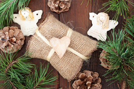 Christmas gift wrapped in natural fabric, decorated with gingerbread heart, angels and pine twigsの写真素材