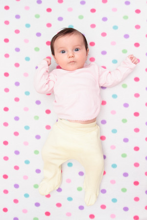 Top view of little baby lying on blanket with colourful polka dotsの写真素材