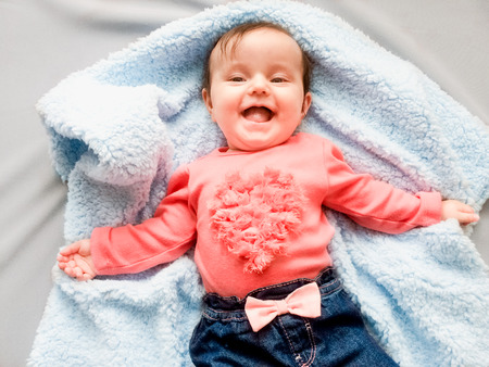 Happy smiling baby girl lying on blue blanketの写真素材