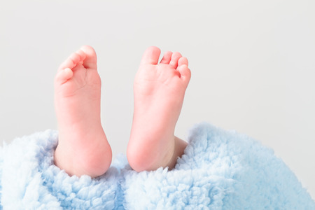 Closeup of baby feet lying on blue blanket. Space for text above. Plain backgroundの写真素材