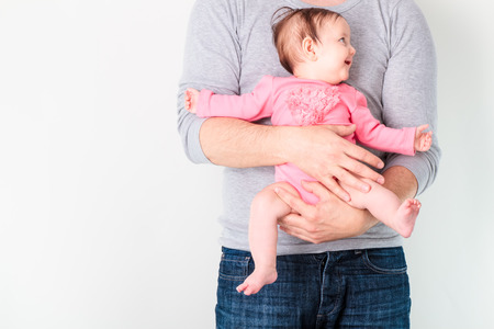 Father holding his smiling daughter. Baby is wearing pink body suit and looking at right sideの写真素材