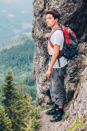 Boy standing on the rocks in the mountains and looking at a valleyの写真素材