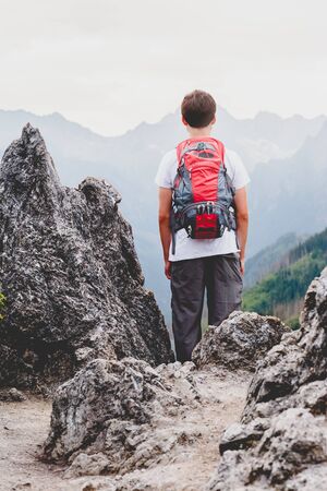 Boy standing on the rocks in the mountains and looking at a valleyの写真素材