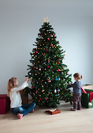 Young girl and her little sister decorating Christmas tree at homeの写真素材