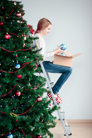 Young girl decorating Christmas tree with balls at homeの写真素材