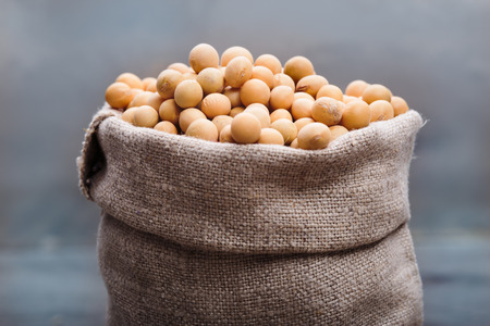 Soya beans in a sack on wooden tableの写真素材