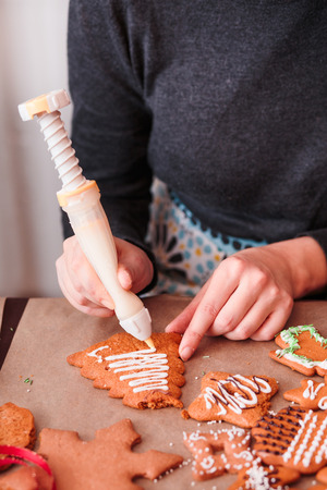 Woman decorating baked Christmas gingerbread cookies with frostingの写真素材