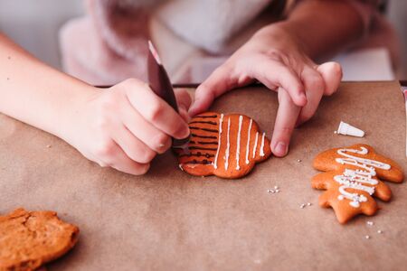 Girl decorating baked Christmas gingerbread cookies with chocolate writing penの写真素材