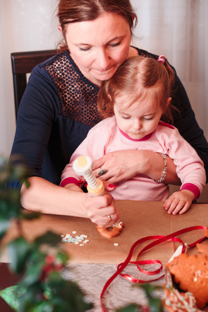 Woman decorating baked Christmas gingerbread cookies with frosting with her little daughterの写真素材