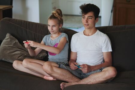 Concentrated young boy and girl playing video games sitting on sofa at homeの写真素材