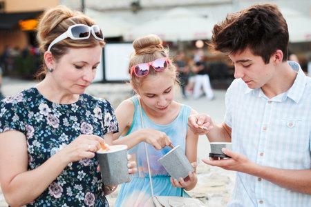 Family spending time together in the city center enjoy eating ice cream on a summer day. Mother,...