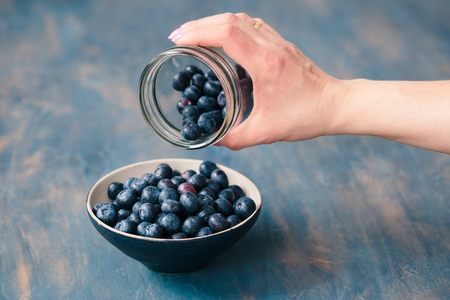 Woman putting freshly gathered blueberries from a jar into a small bowl. Table painted in blue in the backgroundの写真素材