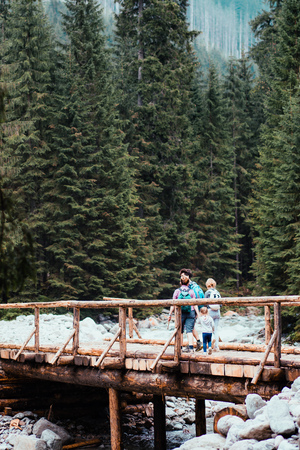Family walking across a wooden bridge over a mountain stream. Spending vacation on wandering with backpacks in a mountains and forestsの写真素材
