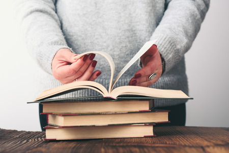 Young woman turning pages of old book on wooden table in antique bookstore. Woman wearing grey sweater and jeansの写真素材
