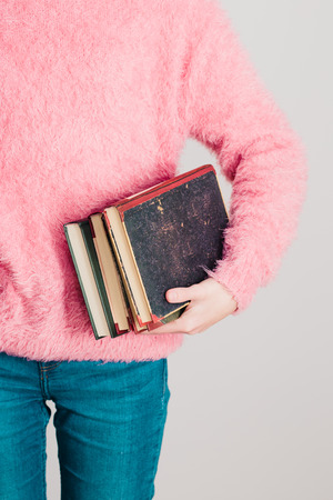 Young girl holding a few books. Teenager girl wearing pink sweater and blue jeans. Vertical photoの写真素材