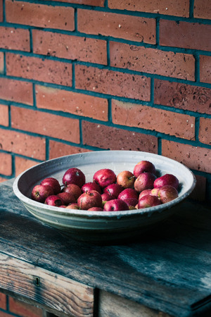 Closeup of big bowl of fresh red apples sprinkled raindrops on wooden tableの写真素材