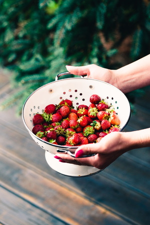 Female hand holding bowl of fresh strawberries sprinkled raindrops over wooden tableの写真素材