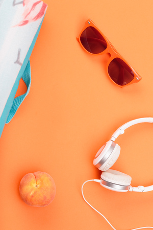 Sunglasses, glass with drink, headphones, peach, blanket on orange background. Minimal summer styleの写真素材