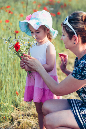 Mother and her little daughter in the field of wild flowers. Little girl picking the spring flowers for her mom for Mother's Day in the meadow. Nature scene, family timeの写真素材